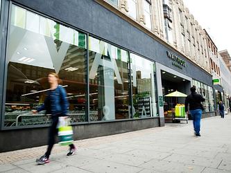 Shoppers walk past a Waitrose supermarket